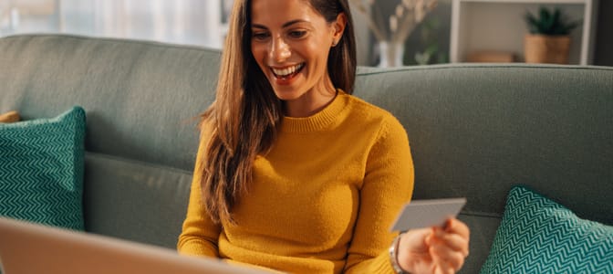 Woman smiling while holding a debit card at home on a blue graphic background