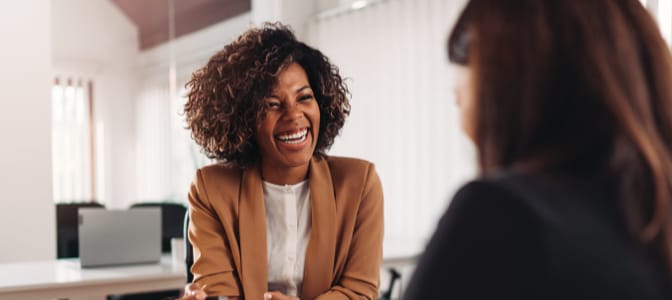 A smiling African American woman speaking to someone at her desk.