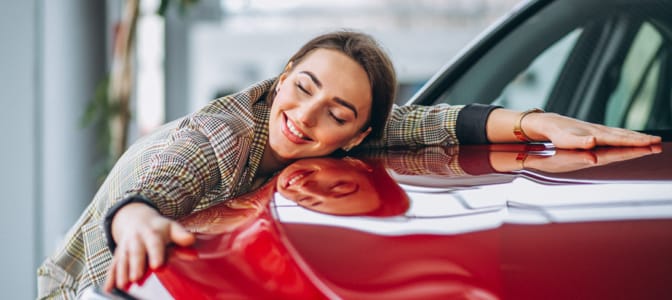 Woman smiling and embracing a new red car at a dealership.