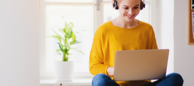 A smiling young woman student on her laptop with headphones.